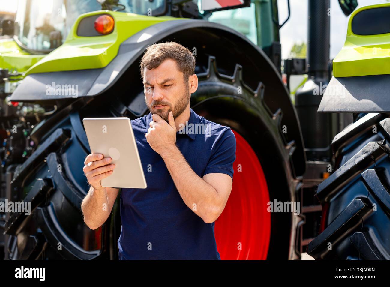 Thoughtful man analyzing information on digital tablet near tractor Stock Photo