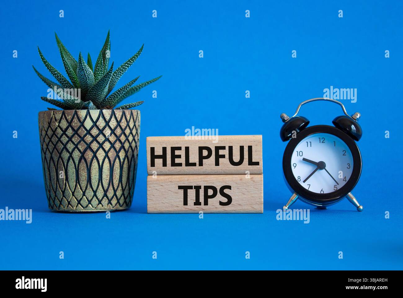 Helpful tips symbol. Wooden blocks with words Helpful tips. Beautiful blue background with alarm clock and succulent plant. Business and Helpful tips Stock Photo