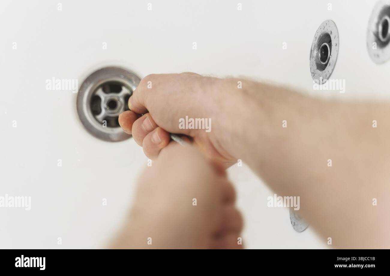 Plumber using drain snake to unclog bathtub Stock Photo