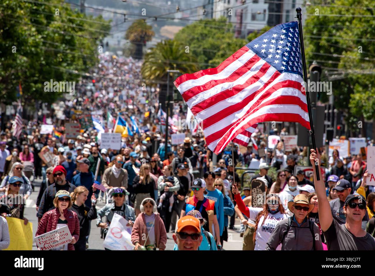 San Francisco, USA. 14th June 2025. A crowd of thousands of protesters march down Market Street with an American flag in the foreground and more flags, including Ukranian flags, are seen in the distance. Credit: Shelly Rivoli/Alamy Live News - Stock Image