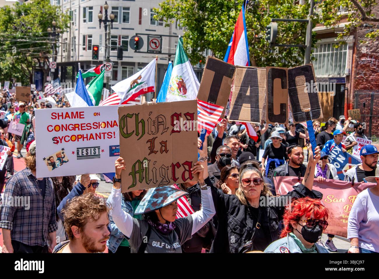 San Francisco, USA. 14th June 2025. Protesters march down crowded Market Street for the No Kings Day protest, with signs reading, 'Shame on congressional sycophants!' 'Chinga la Migra,' and 'TACO,' with a mix of American, Mexican, and California flags in the distance  Credit: Shelly Rivoli/Alamy Live News - Stock Image