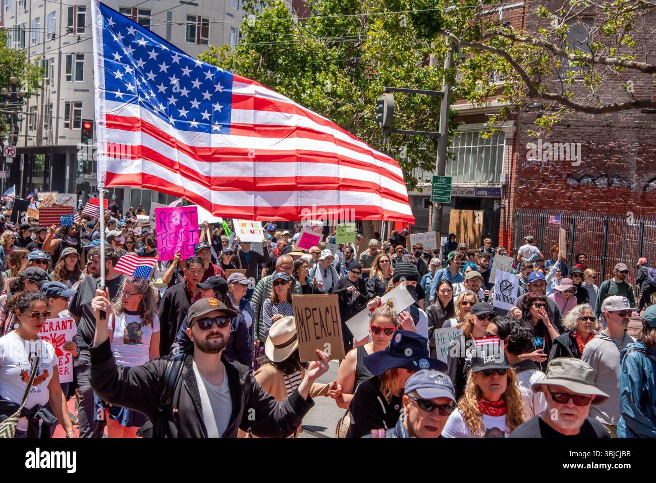 San Francisco, USA. 14th June 2025. Among the many protesters marching in the No Kings Day event in San Francisco, one man holds an American flag above his head with one hand and a sign reading, 'IMPEACH' in the other.  Credit: Shelly Rivoli/Alamy Live News - Stock Image