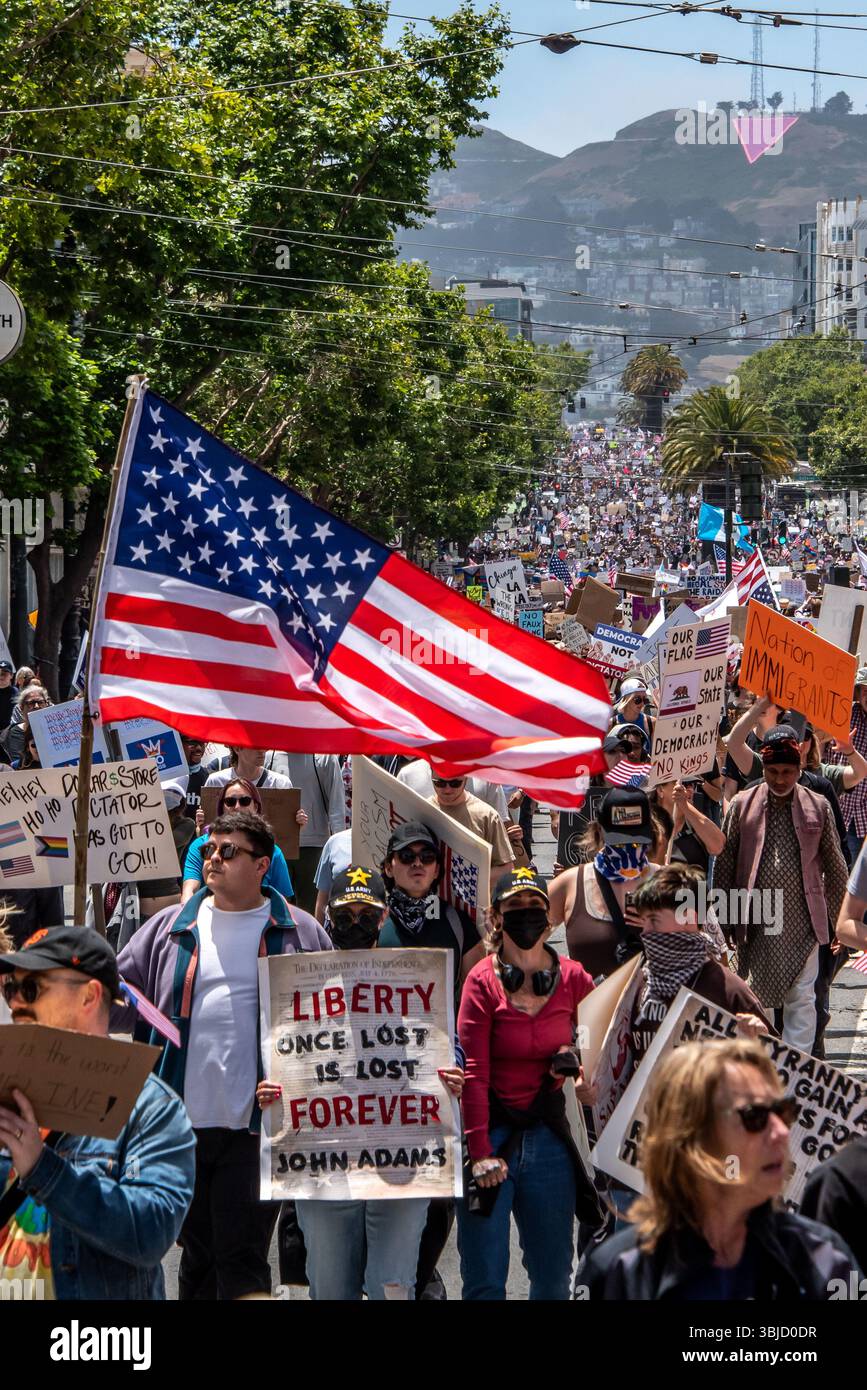 San Francisco, USA. 14th June 2025. In the foreground of the massive crowd of protesters marching in the No Kings Day protest, an American flag flies above a protester with a sign reading, 'Liberty once lost is lost forever,' a quote attributed to John Adams. Credit: Shelly Rivoli/Alamy Live News - Stock Image