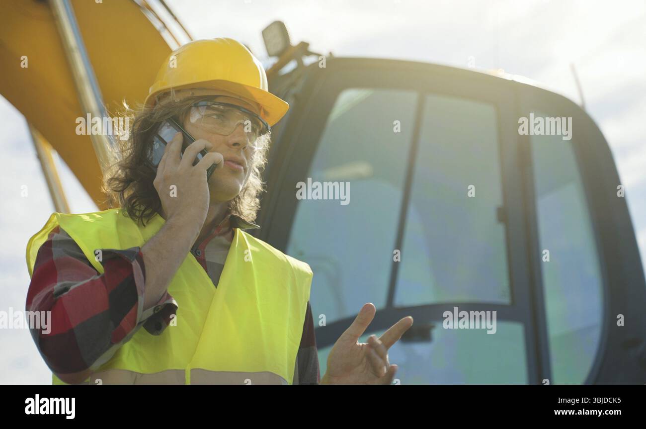 Excavator operator in hard hat talking by smartphone Stock Photo