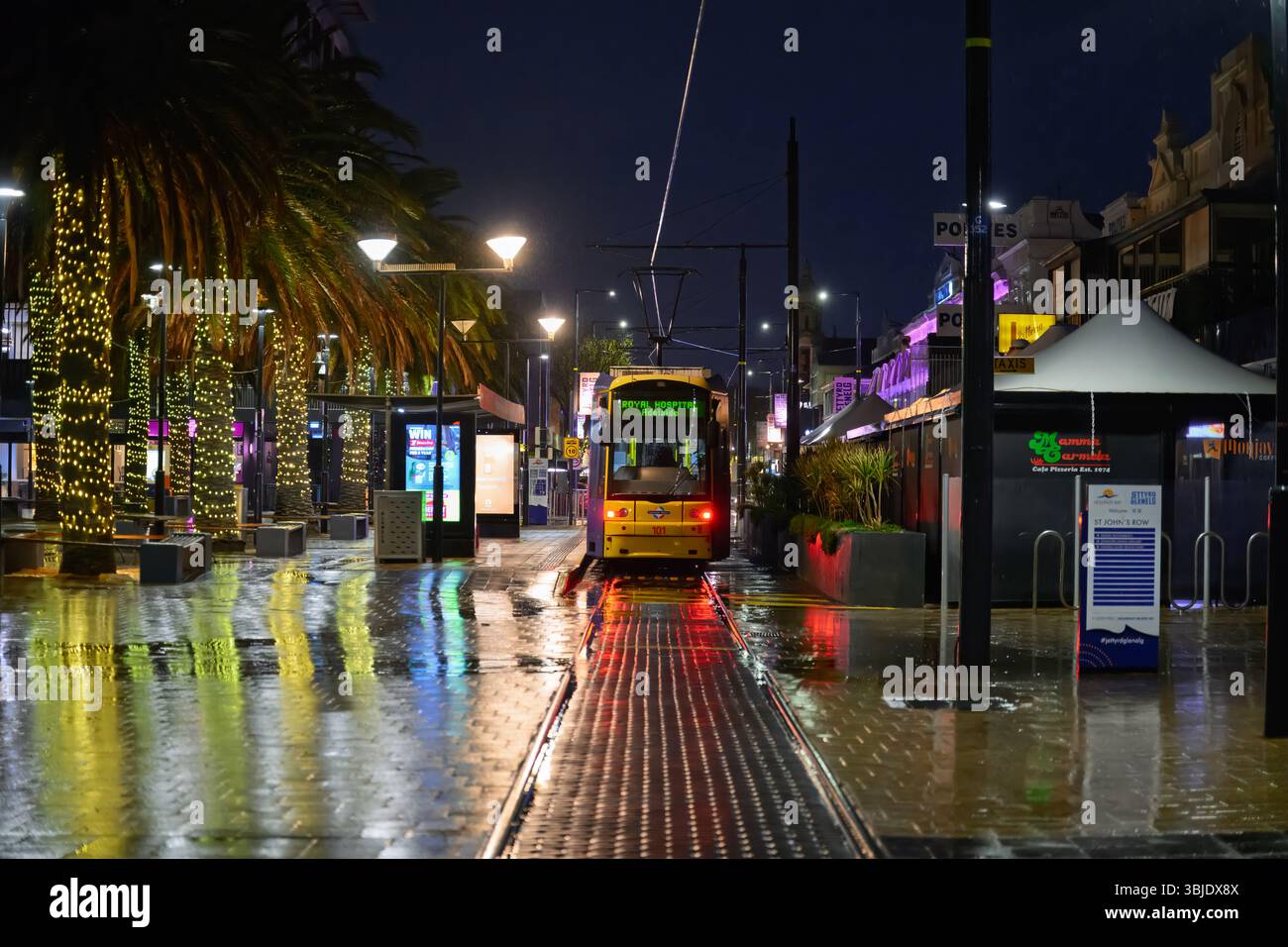 Glenelg, South Australia - June 2025: Tram stop on wet night, with reflections of lights on city streets, public transport in Adelaide Stock Photo