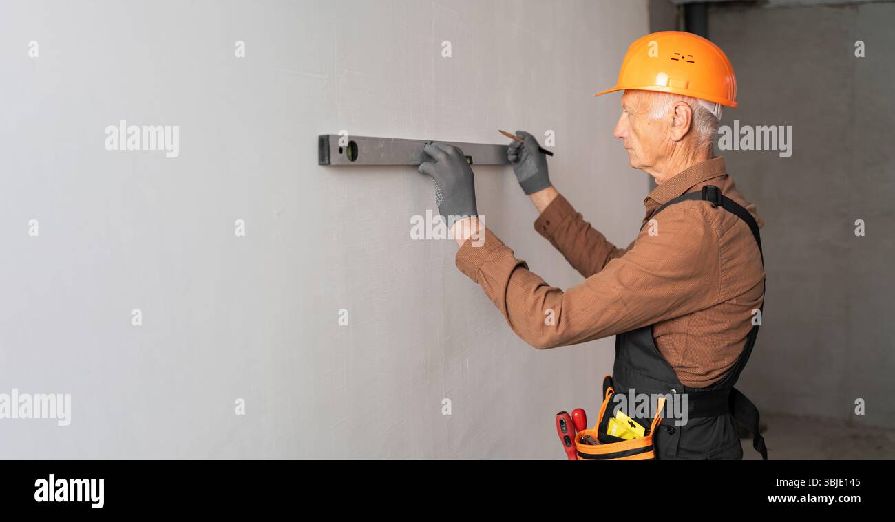 Elderly male builder using spirit level checking the leveling of a wall ...