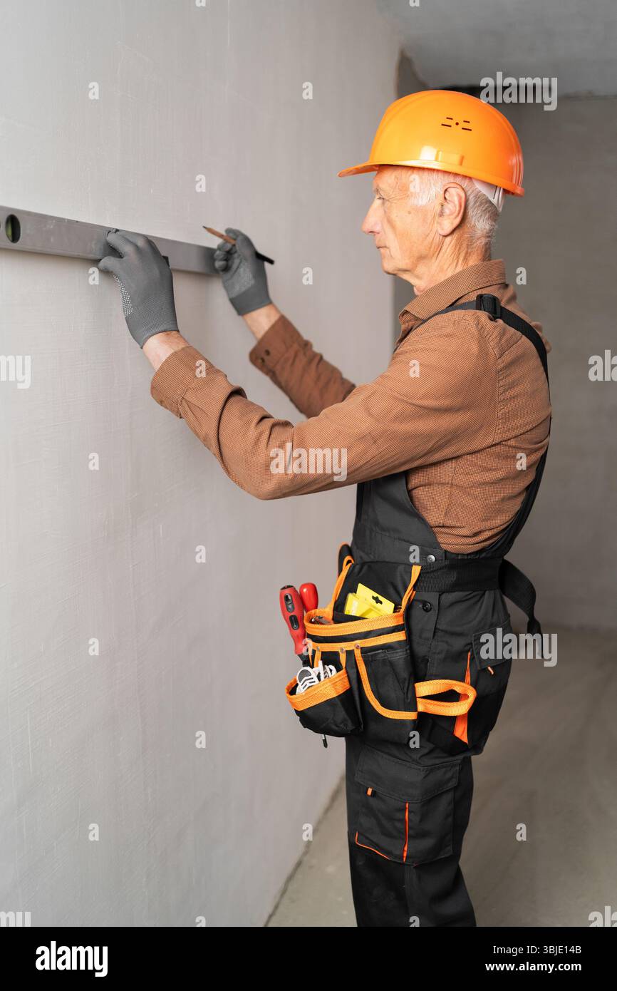 Elderly male builder using spirit level checking the leveling of a wall ...