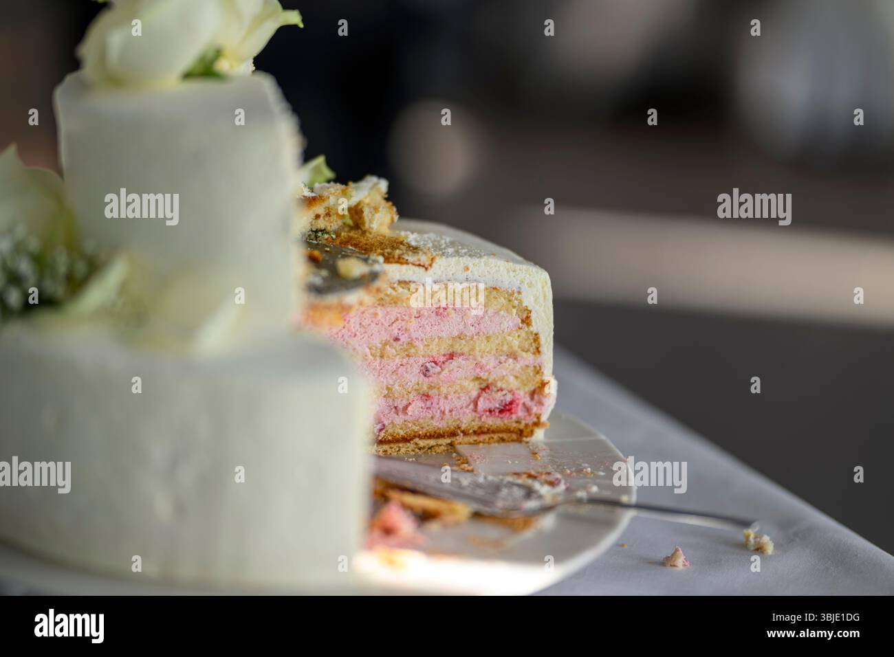 , Deutschland, 14.06.2025,  Detailaufnahme einer angeschnittenen Hochzeitstorte mit weißem Überzug und rosa Sahne- oder Cremefüllung. Zu sehen ist der Stock Photo