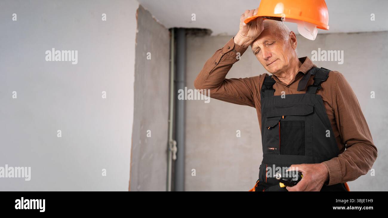 Sad elderly construction worker taking off helmet suffering from depression and job problems at building site Stock Photo