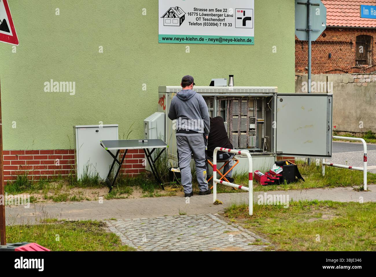 June 10, 2025 – Teschendorf, Germany: Two technicians connect and splice fiber optic cables inside an open telecom cabinet during a rural infrastructu Stock Photo
