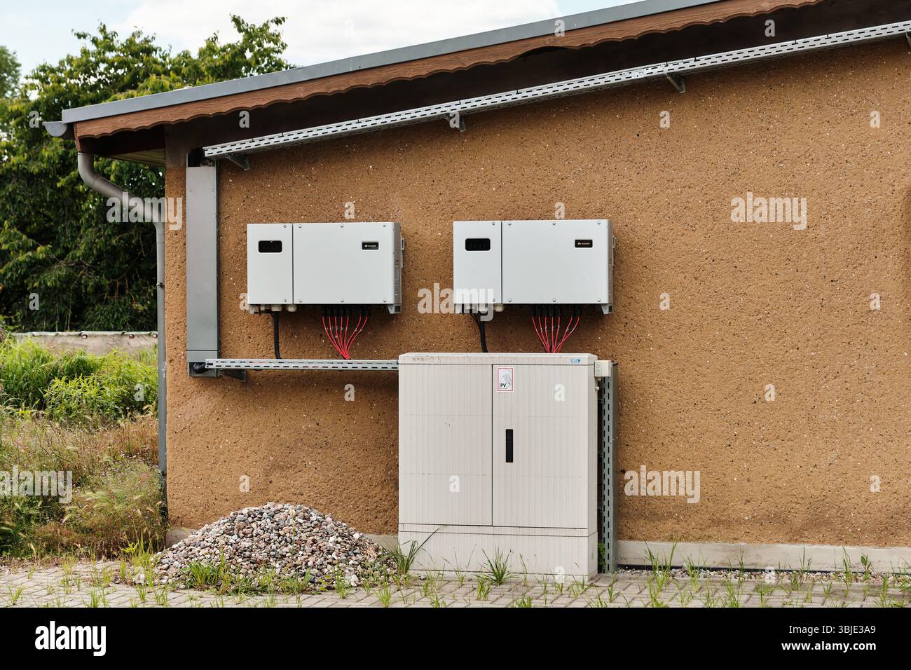 June 12, 2025 - Woldegk-Germany: Two Huawei inverters with red cabling mounted on an exterior wall, connected to a power distribution unit in a rural Stock Photo