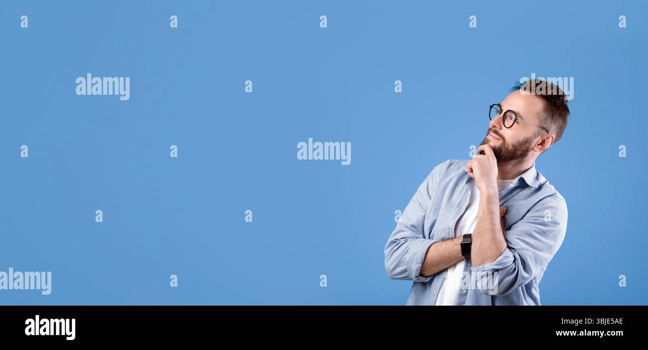 Pensive Caucasian guy thinking over decision or problem, looking at empty space over blue studio background Stock Photo