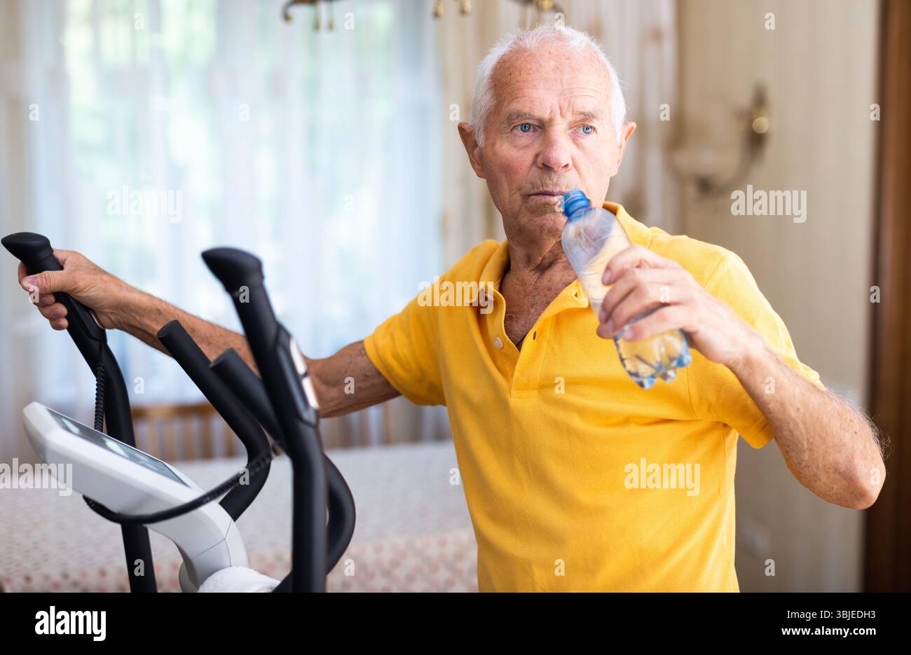 Senior man using elliptical trainer and drinking water Stock Photo