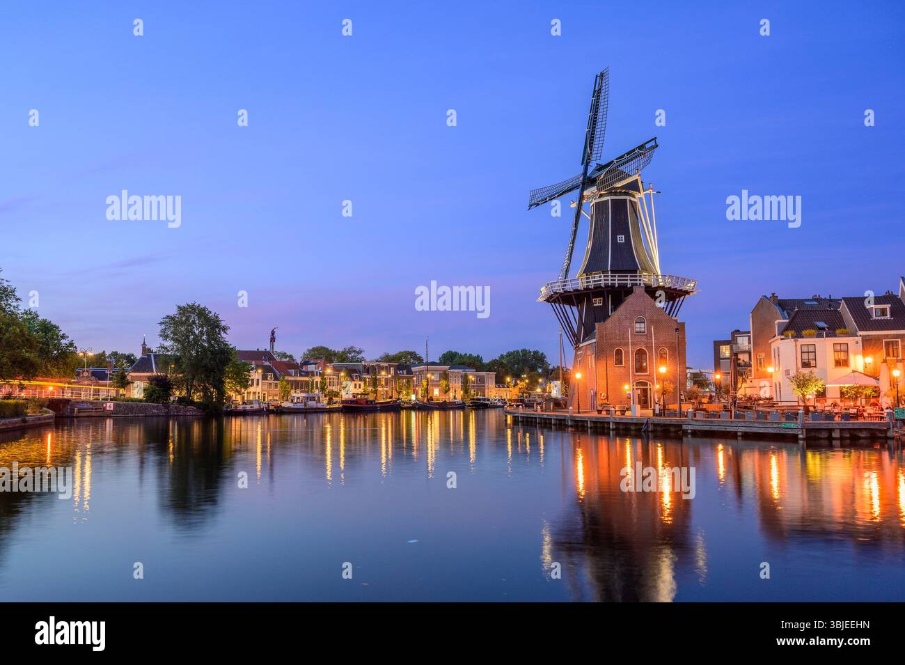 Golden lights illuminate Windmill De Adriaan along the Spaarne River at dusk in Haarlem. Stock Photo