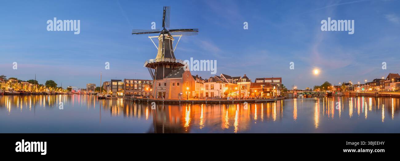 Golden lights illuminate Windmill De Adriaan along the Spaarne River at dusk in Haarlem. Stock Photo