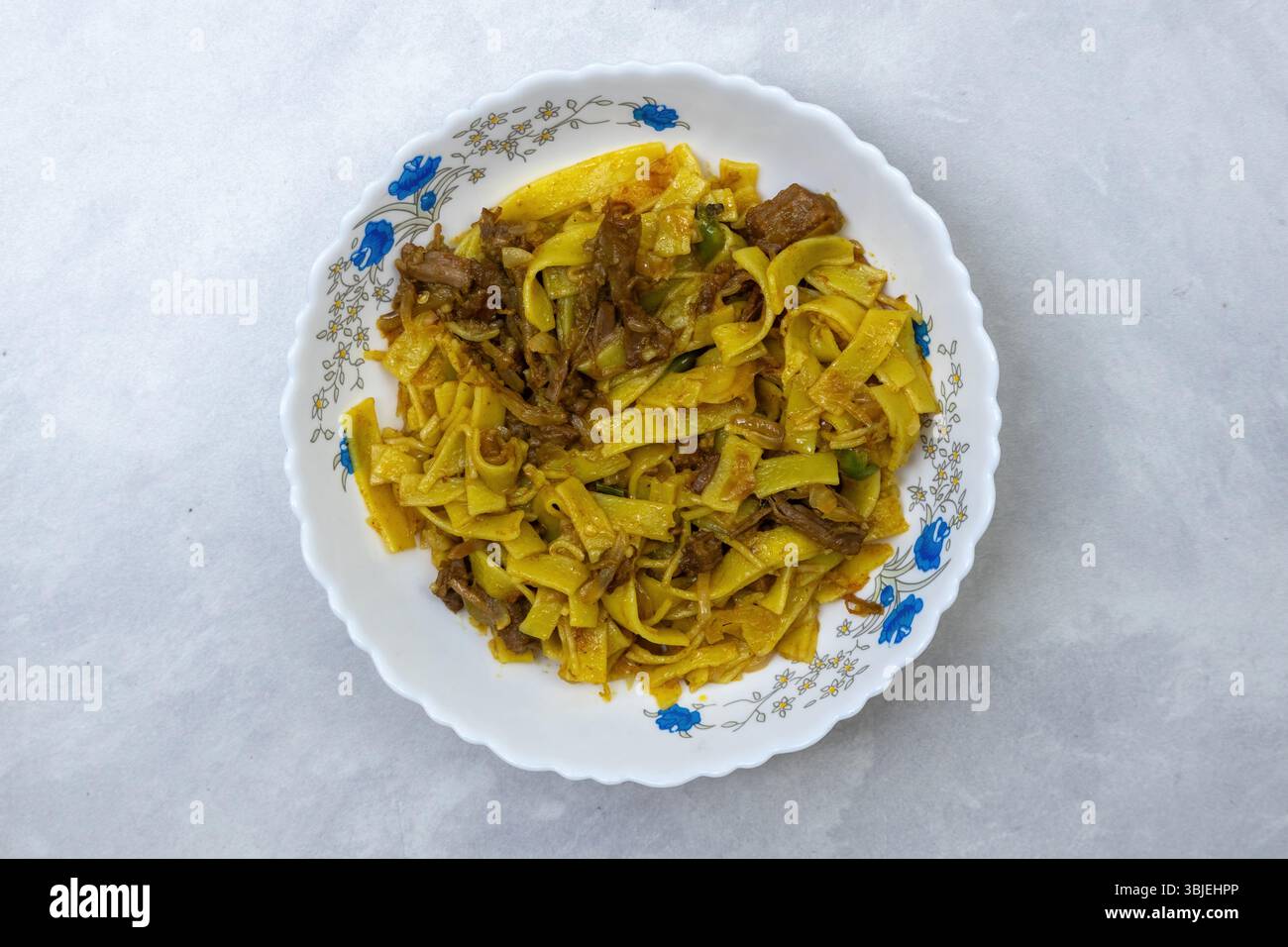 Savory flat noodles with beef, served in white bowl. Appetizing Asian food top view. Stock Photo