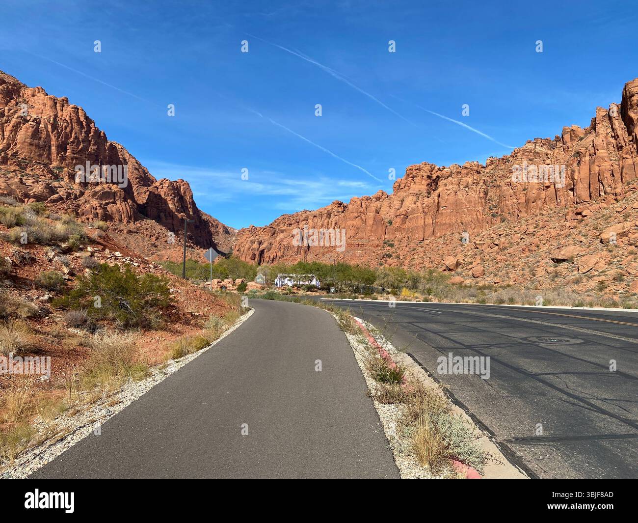 Scenic view of a paved road winding through a landscape dominated by towering red rock formations under a clear, bright blue sky in St. George, Utah. - Smartphone Captured Stock Image