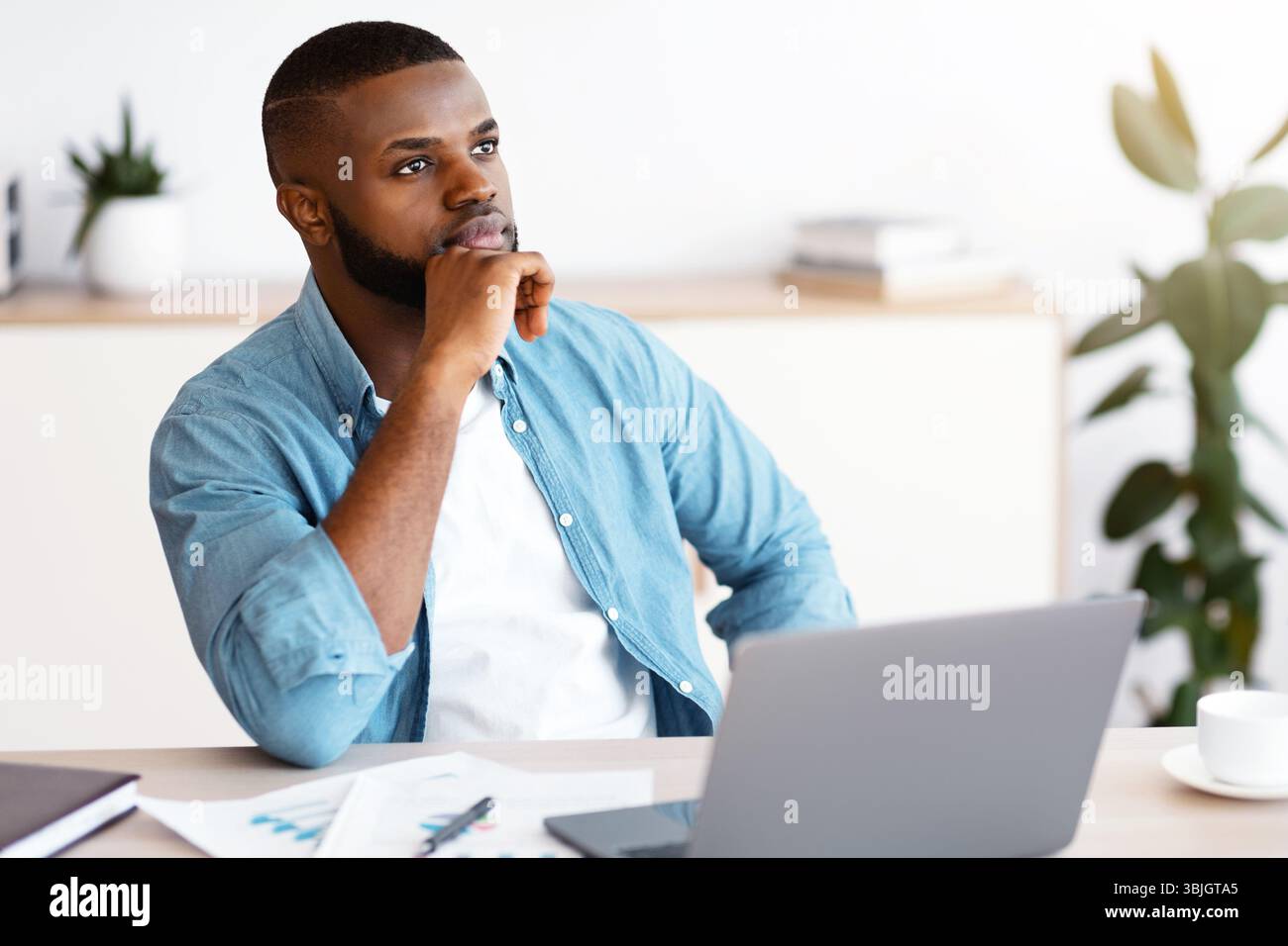 Black Freelancer Guy Sitting At Workplace With Thoughtful Face Expression Stock Photo