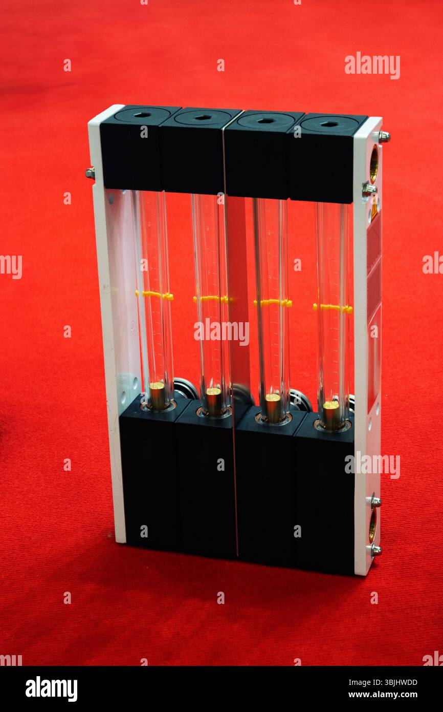 Multi-tube rotameter flow meter with four glass tubes and yellow floats against a red background, used for measuring gas or liquid flow rates in labor Stock Photo