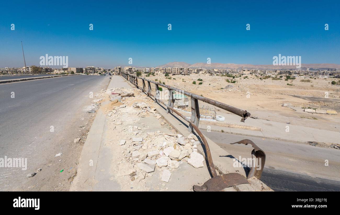 Damege Railing A deserted road with damaged railing and debris, overlooking a barren ...