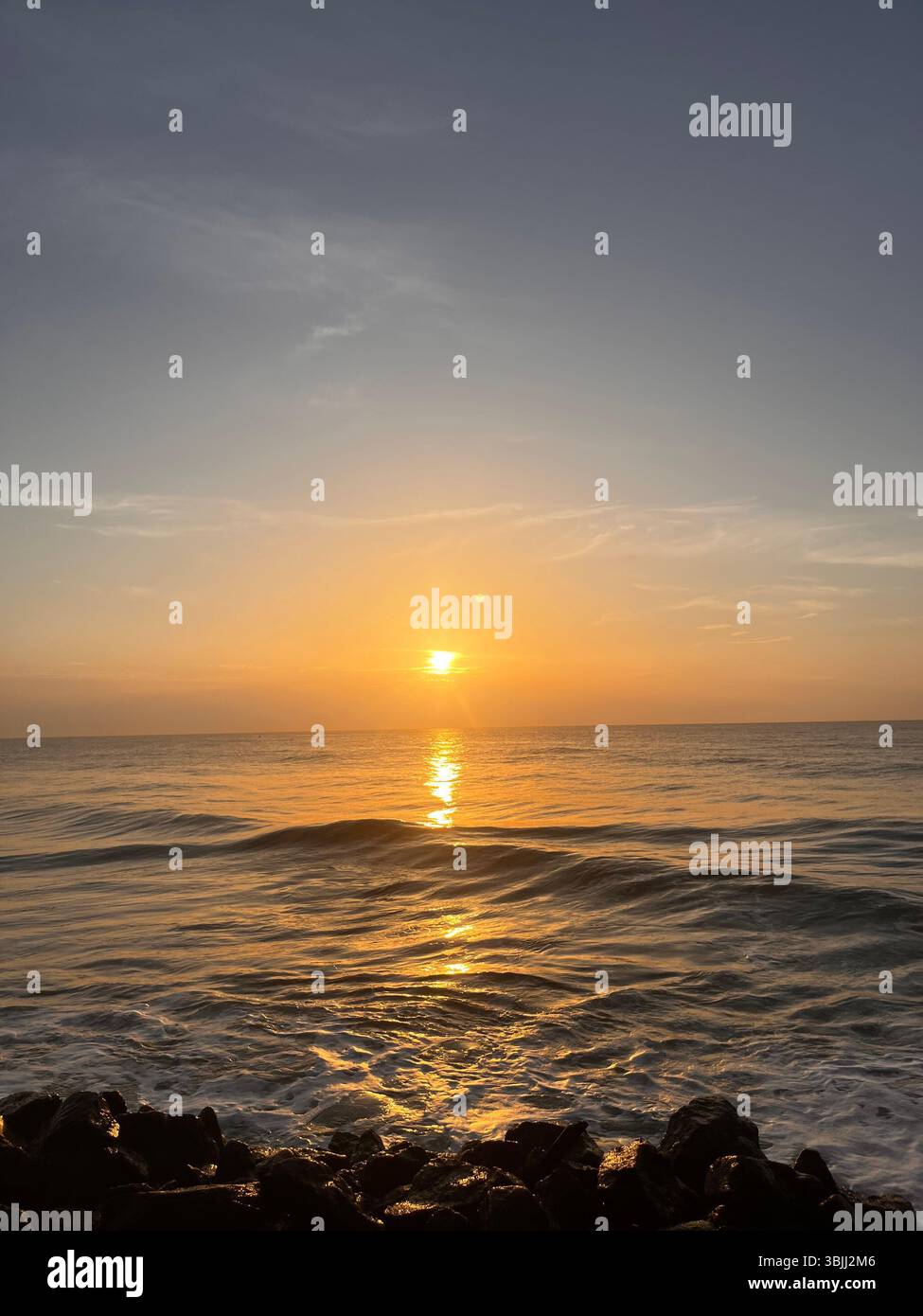 Beautiful sunrise over the ocean with waves and blue skies. - Smartphone Captured Stock Image