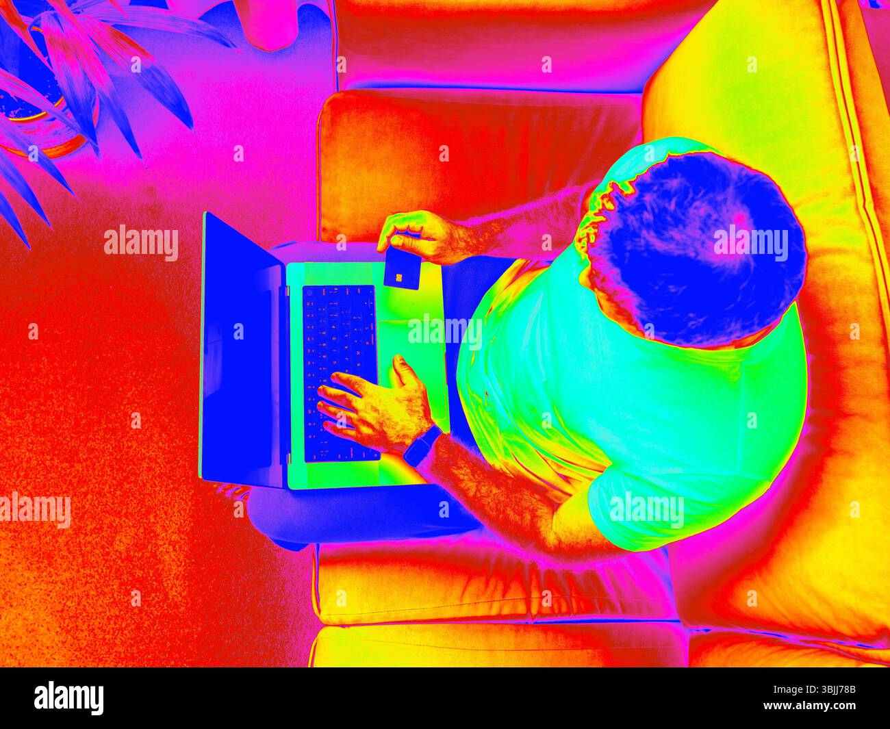 Infrared Thermal Image of man using laptop in living room interior. Overhead shot of man entering bank card information on laptop in modern minimalist living room Stock Photo