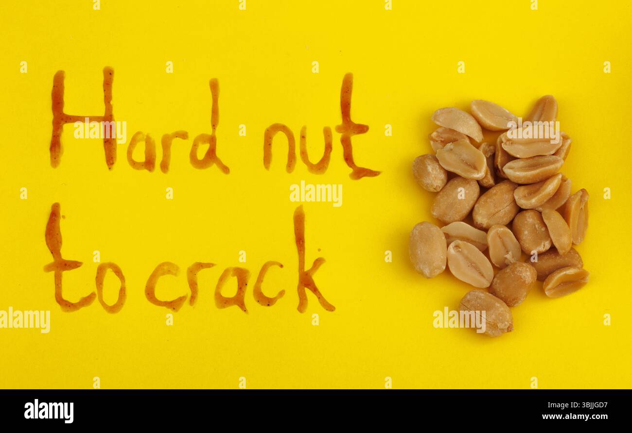 Caramelized peanuts on a yellow background with the words hard nuts to crack Stock Photo
