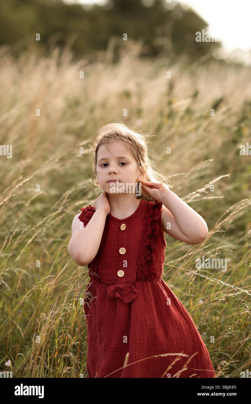 Child girl standing in high grass field and touching her hair. Stock Photo