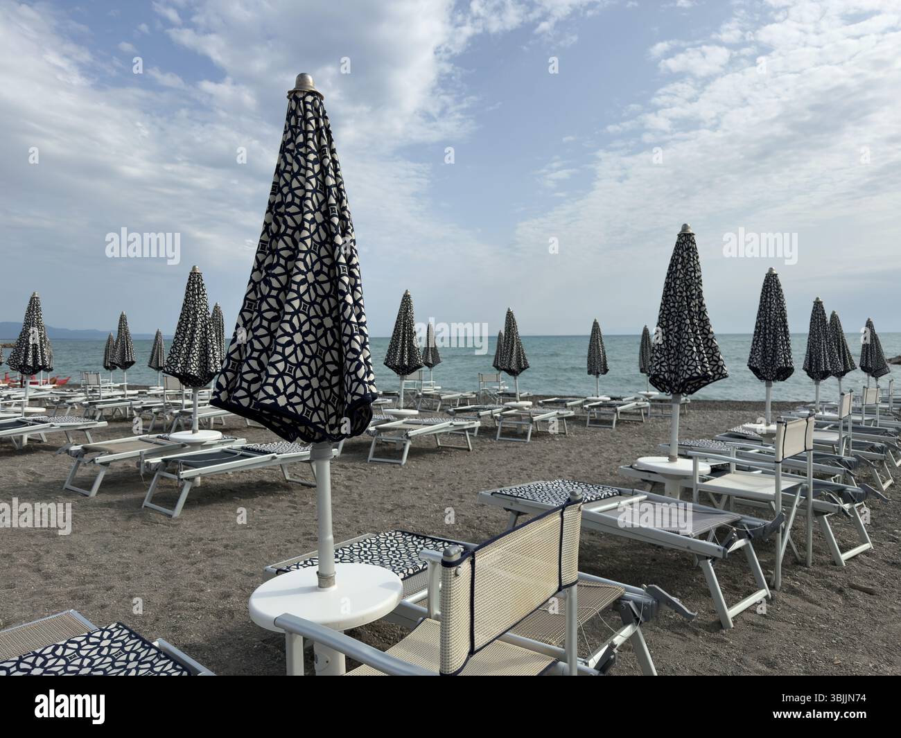 Closed umbrellas and sun loungers on the morning beach against the backdrop of the sea shoreline - Smartphone Captured Stock Image