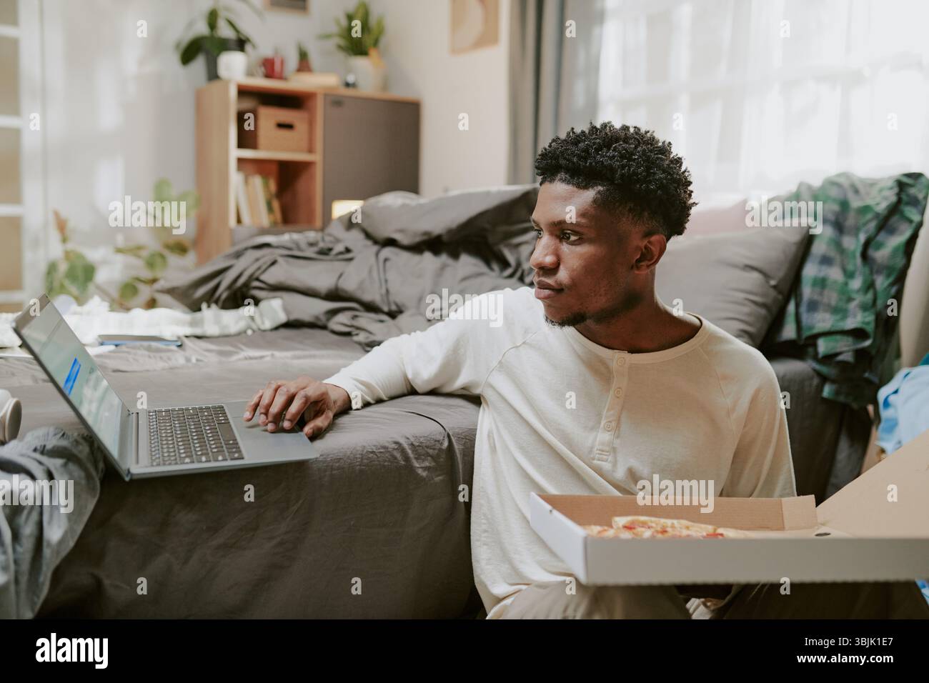 Young Man Using Laptop While Sitting on Bed Stock Photo