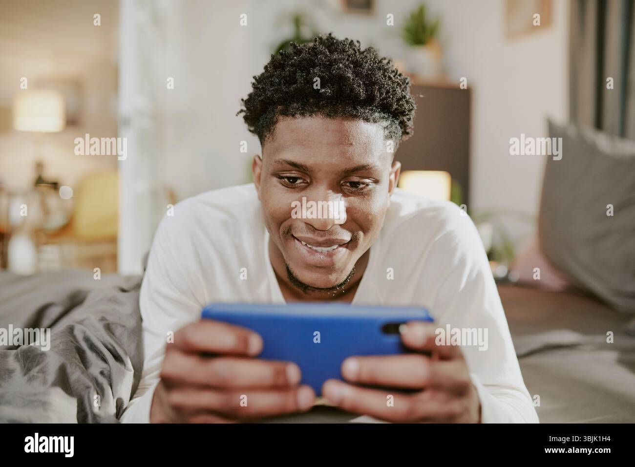 Smiling Man Using Smartphone in Cozy Indoor Setting Stock Photo