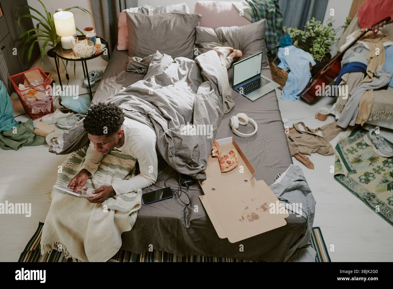 Working on Tablet While Lying on Bed Surrounded by Clutter Stock Photo