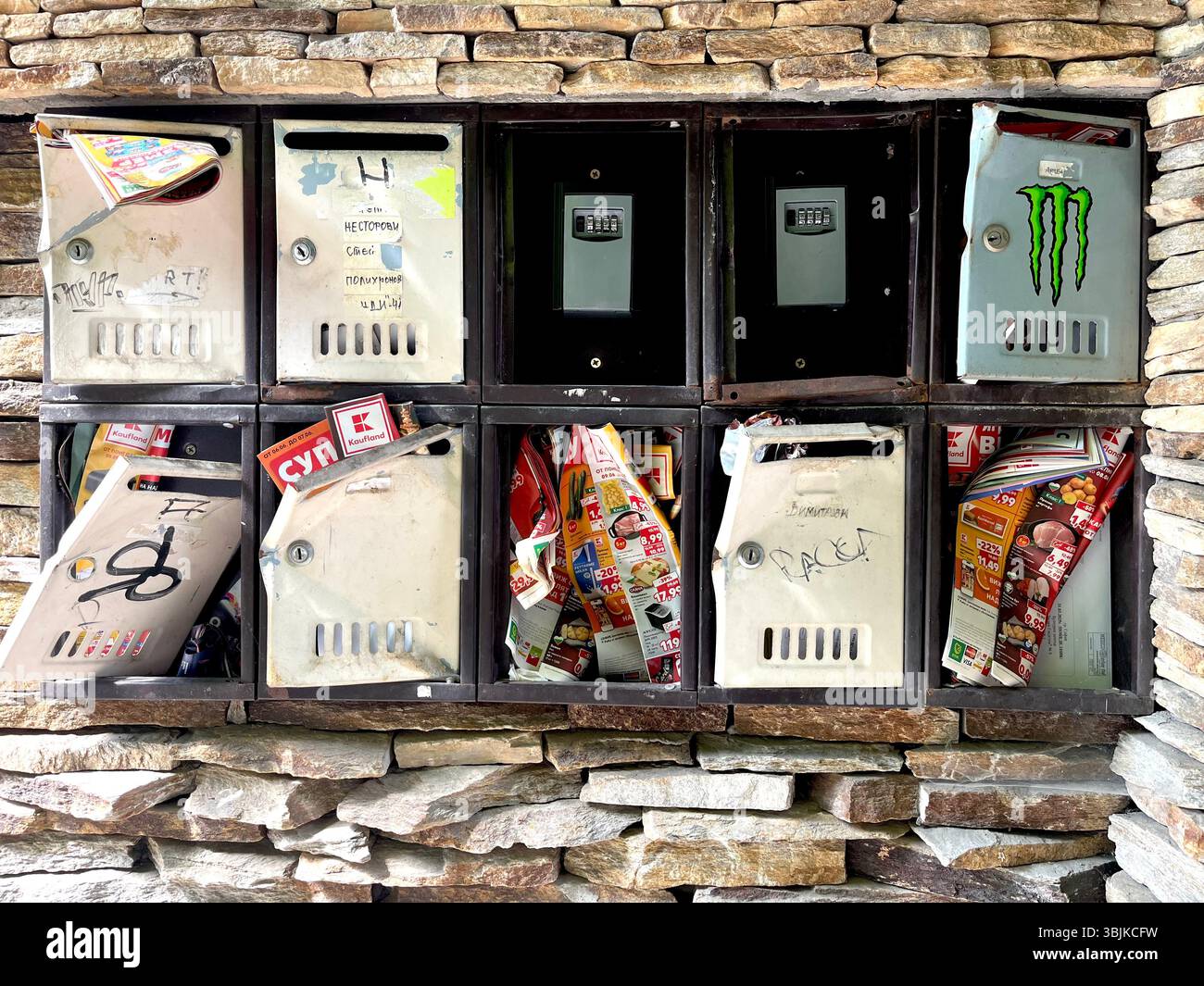 Outdoor postboxes mounted on stone wall of residential building, with some broken units and several key lockboxes for self check-in short-term rentals - Smartphone Captured Stock Image