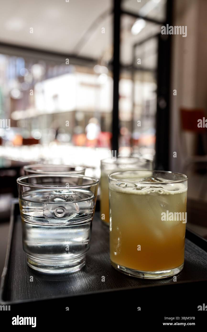 Glasses of iced juice and water on tray with blurred city street view behind glass. Stock Photo