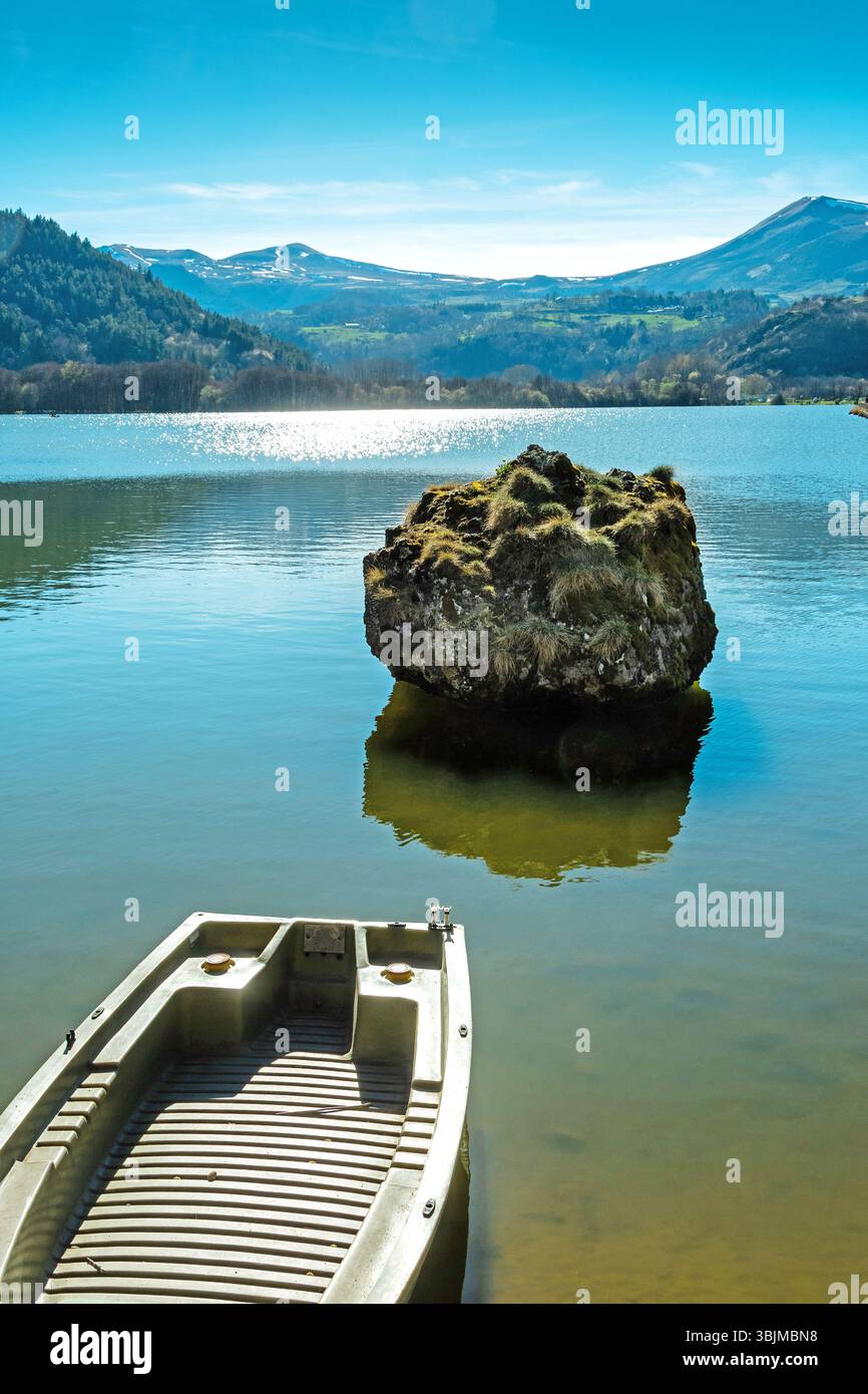 Lake chambon reflects the stunning blue sky and surrounding mountains. A small boat rests at the shore. Puy de Dome. Auvergne. France Stock Photo