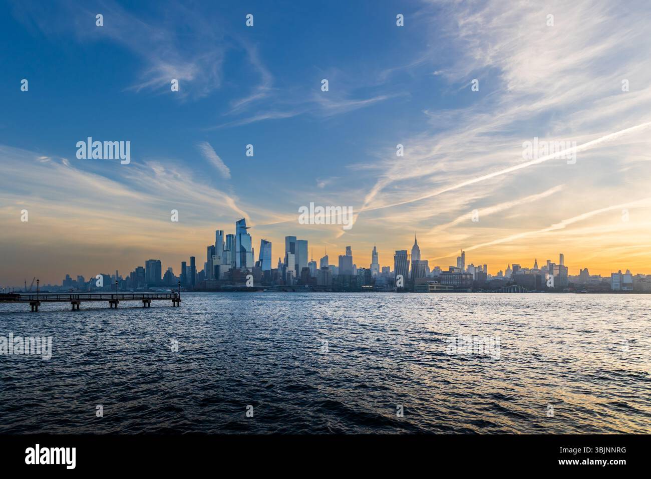 Wide-angle view of Manhattan skyline with layered morning clouds and the soft colors of sunrise reflecting in the Hudson River, captured from Hoboken. Stock Photo