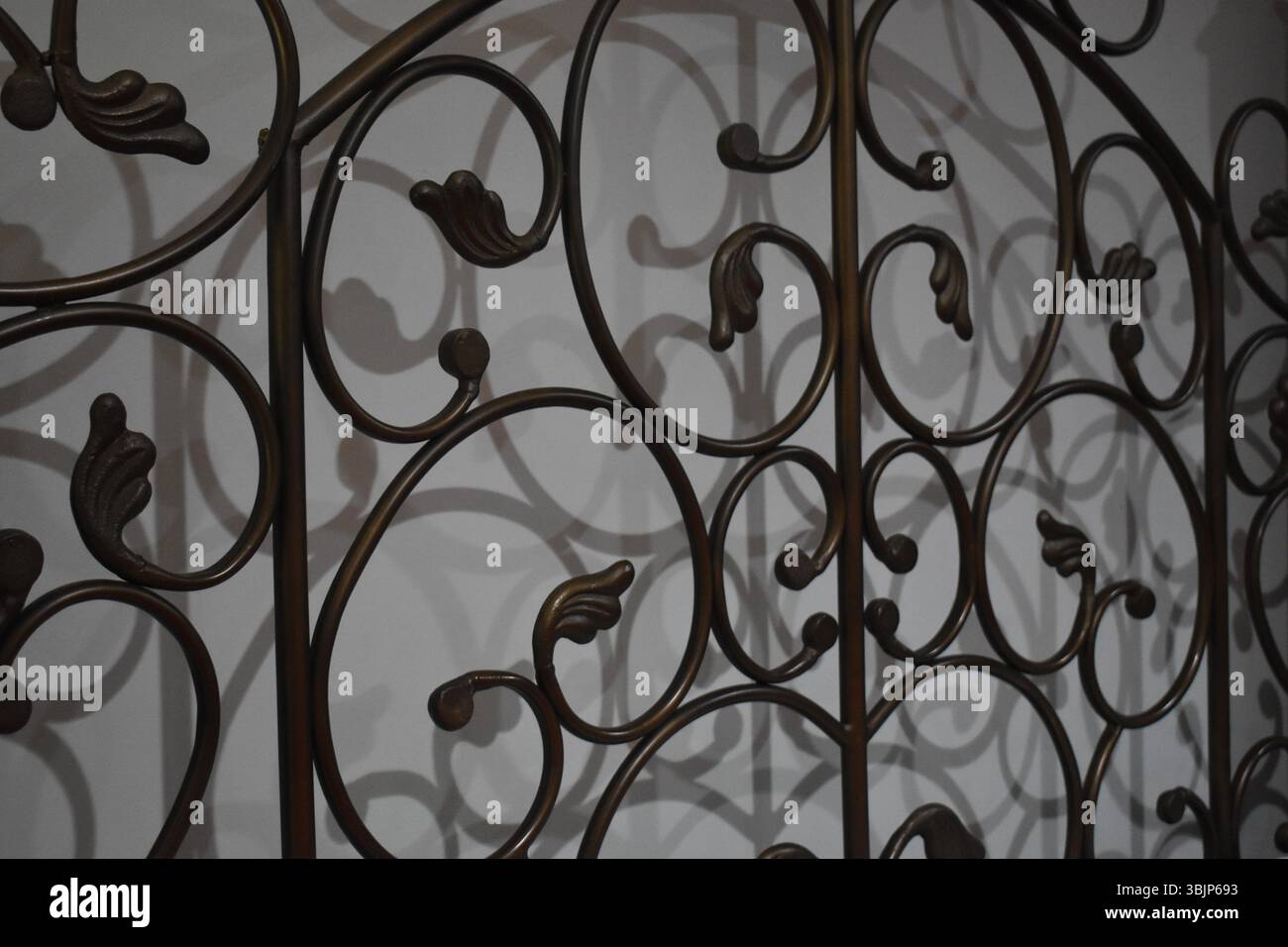 The scrolls on the black-colored metal headboard add an elegant look to the room.  The shadow of the design on the white wall behind the bed makes an Stock Photo
