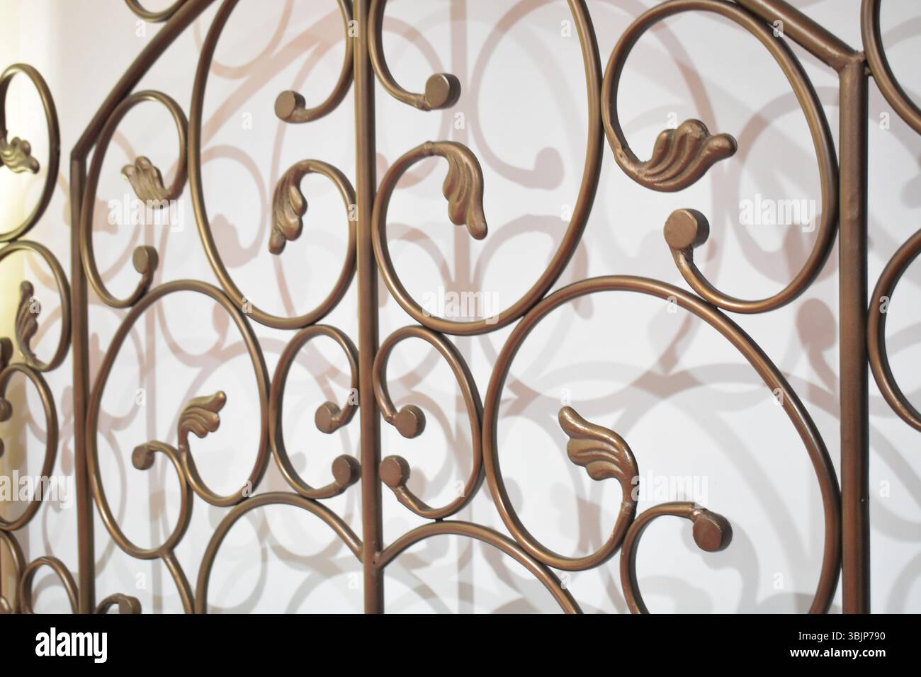 The scrolls on the black-colored metal headboard add an elegant look to the room.  The shadow of the design on the white wall behind the bed makes an Stock Photo