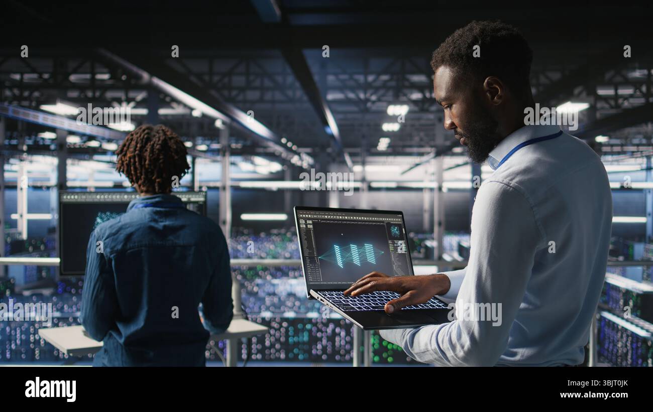 Server hub coworkers visualizing large language model architecture using notebook. Data center technicians on industrial platform collaborating on neural network software tasks using laptop Stock Photo