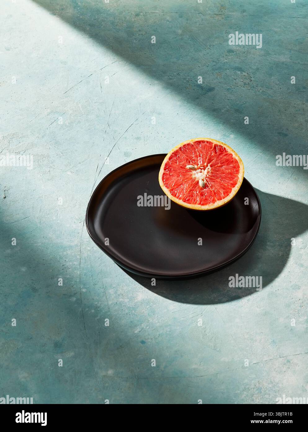 Sliced grapefruit on black plate with blue textured surface Stock Photo