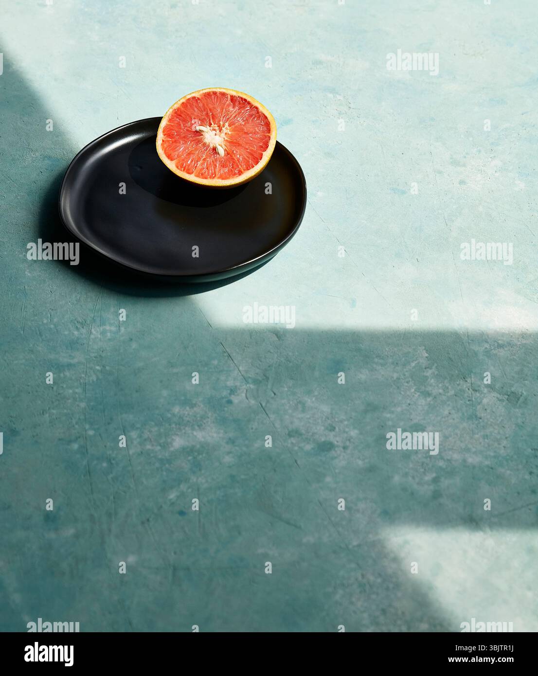 Sliced grapefruit on black plate with blue textured surface Stock Photo