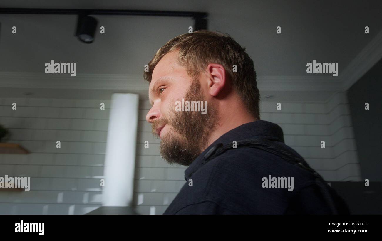 Side profile of a serious bearded police officer in uniform standing indoors with tiled white wall background, focused expression. Stock Photo