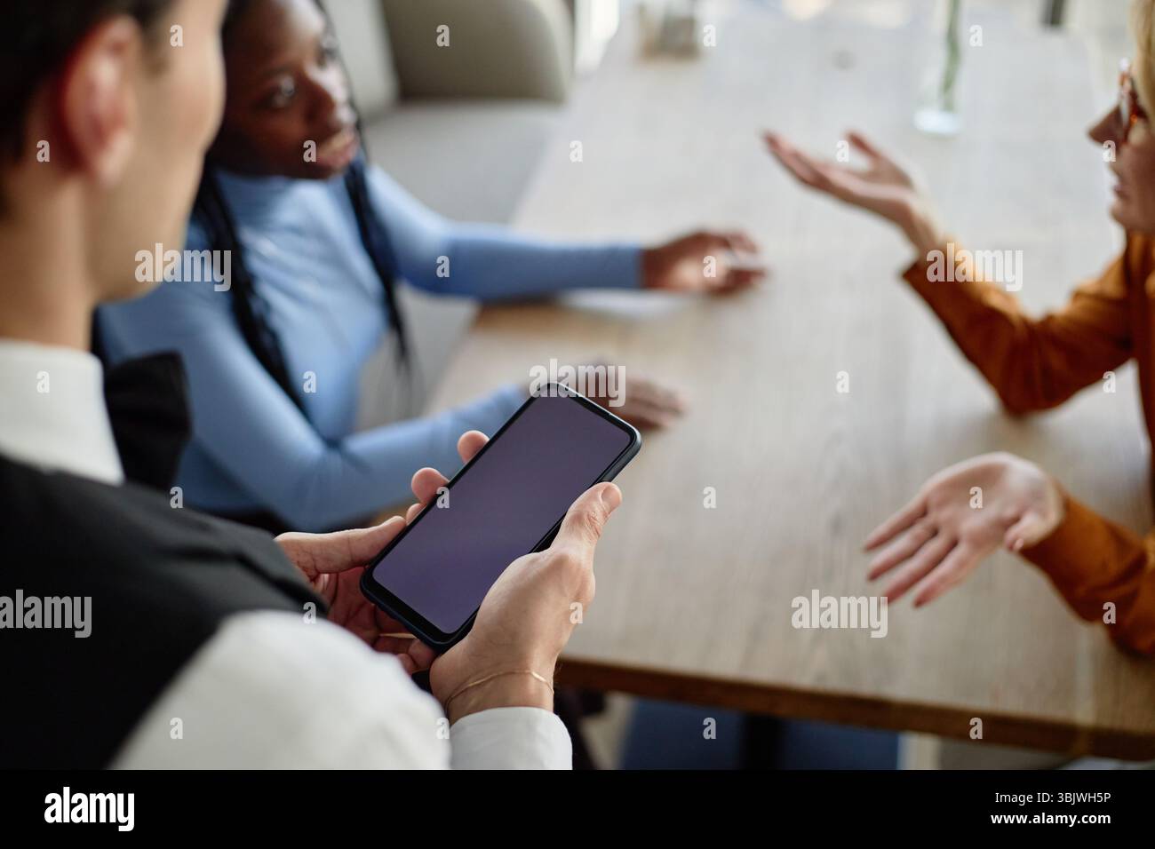 Young Caucasian Man Using Smartphone While Talking with Diverse Clients Stock Photo