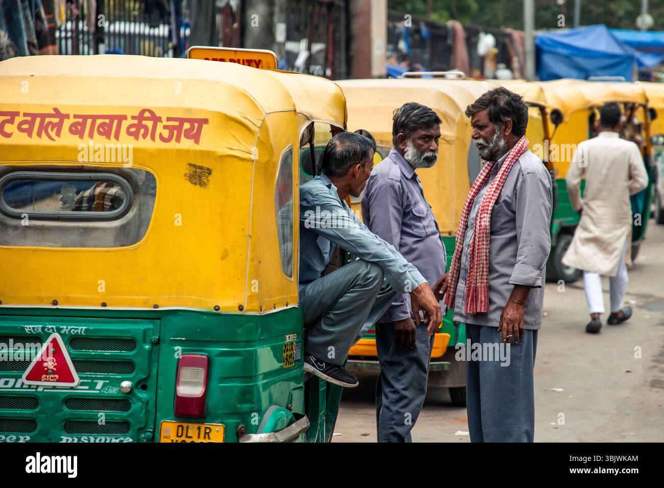 Three auto rickshaw drivers are discussing next to their parked ...