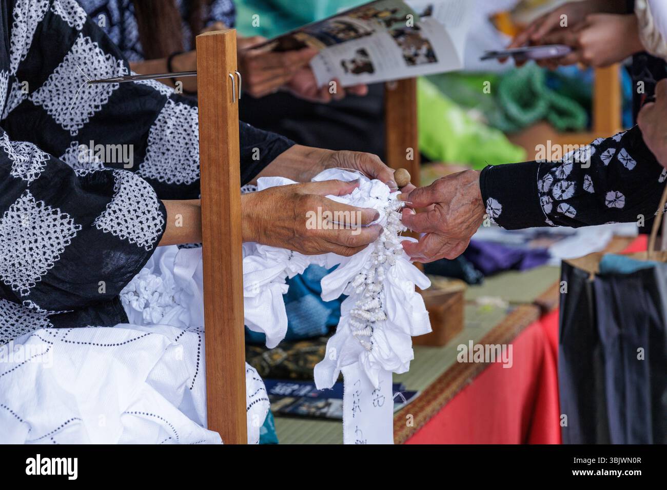 Artisan engages in tying cone shaped knots into fabric used in traditional Japanese Arimatsu-shibori resist-dyeing as part of workshop at festival. Stock Photo