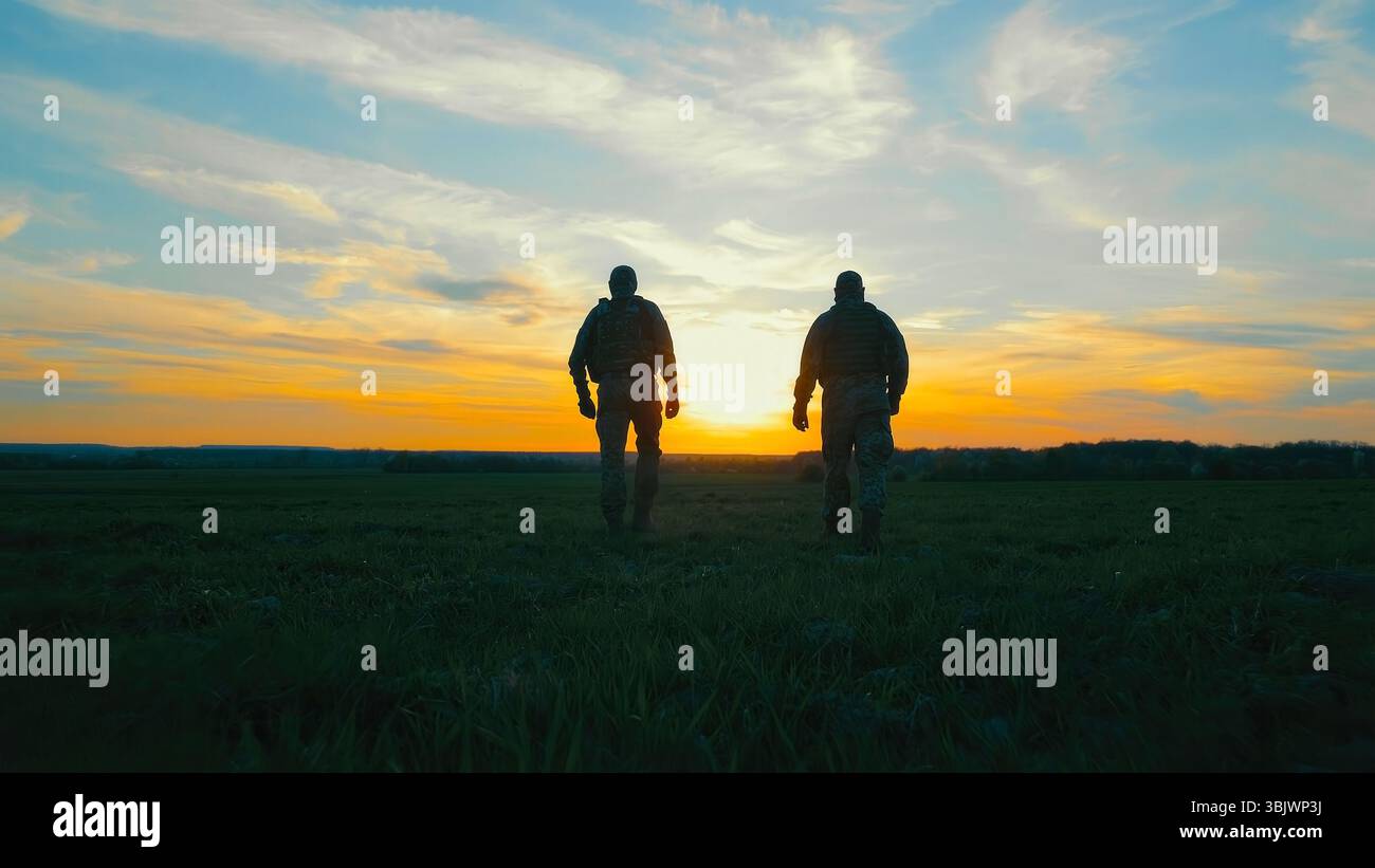 Two soldiers walking across a field at sunset. A dramatic silhouette of two soldiers walking through a field during sunset. Stock Photo