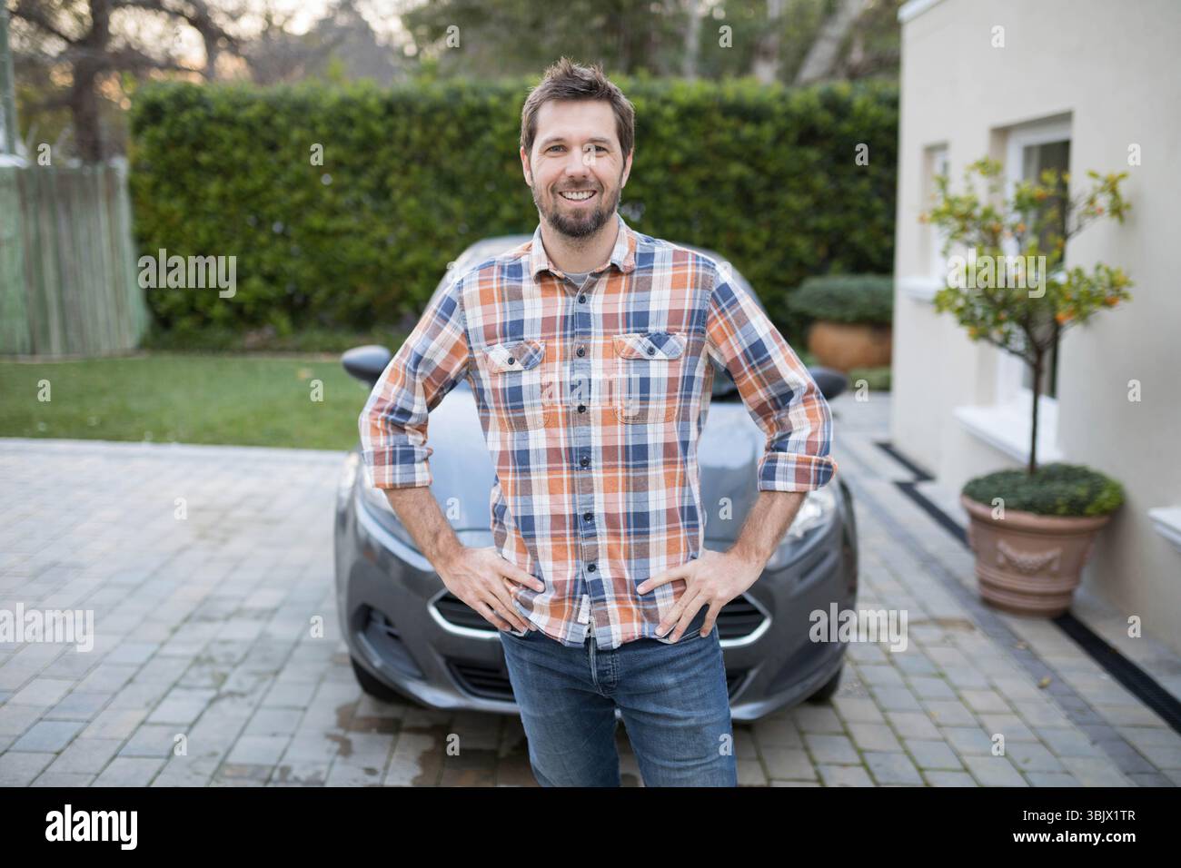Man in his thirties standing confidently on suburban driveway with gray ...