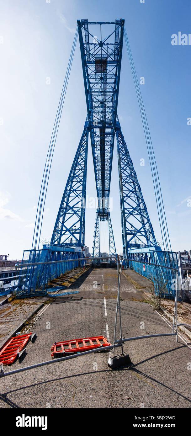tall blue middlesbrough transporter suspension bridge with metal structures against a clear blue sky and a closed pathway below Stock Photo