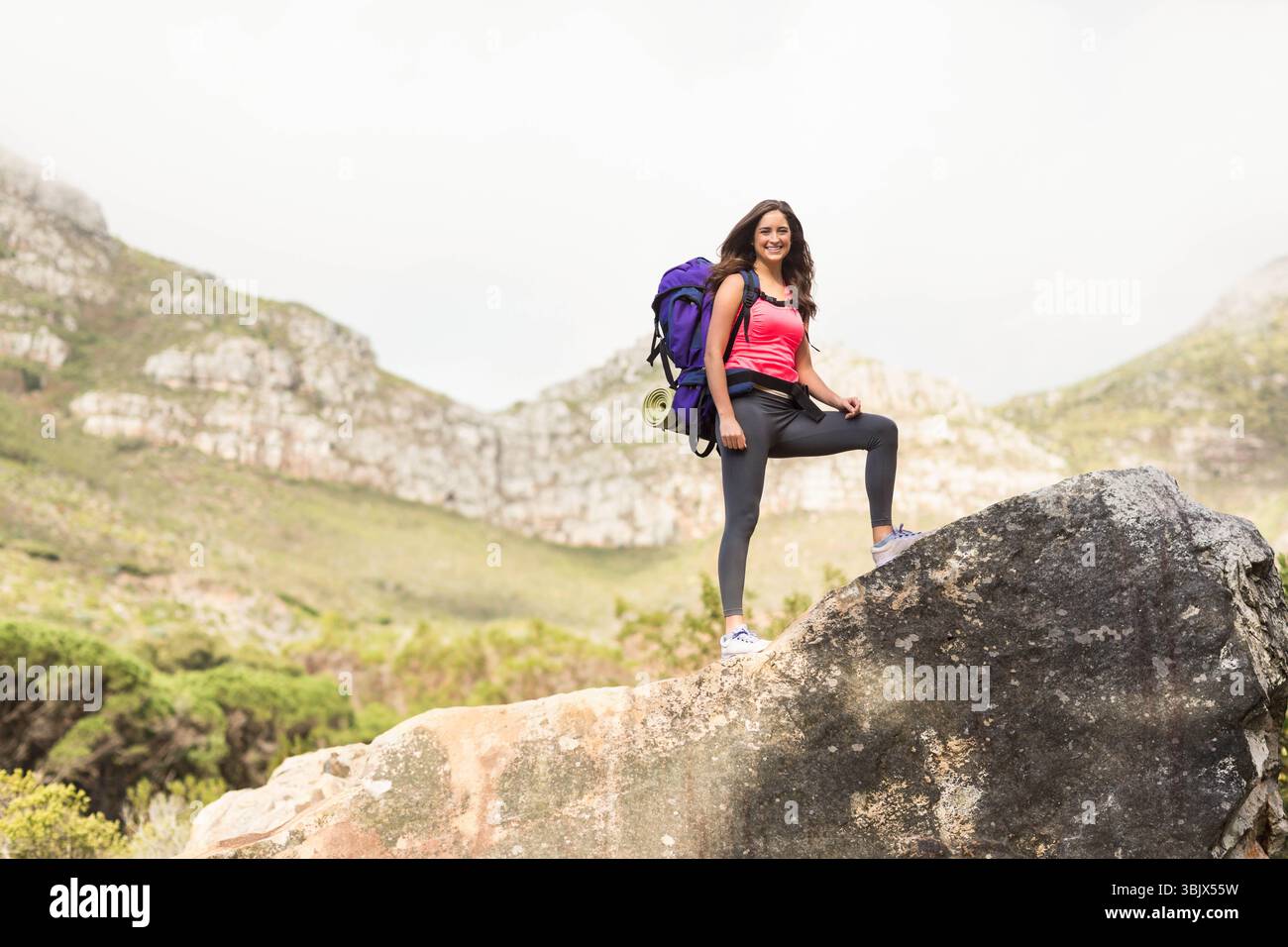 Female hiker standing on boulder at mountain trail with purple backpack and rolled mat, copy space Stock Photo