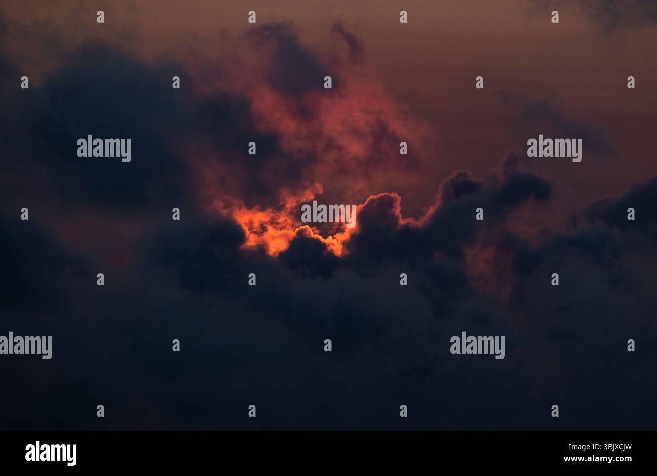 The setting sun lights up gathering clouds with an orange red glow over the ocean, Cornwall, England. Stock Photo